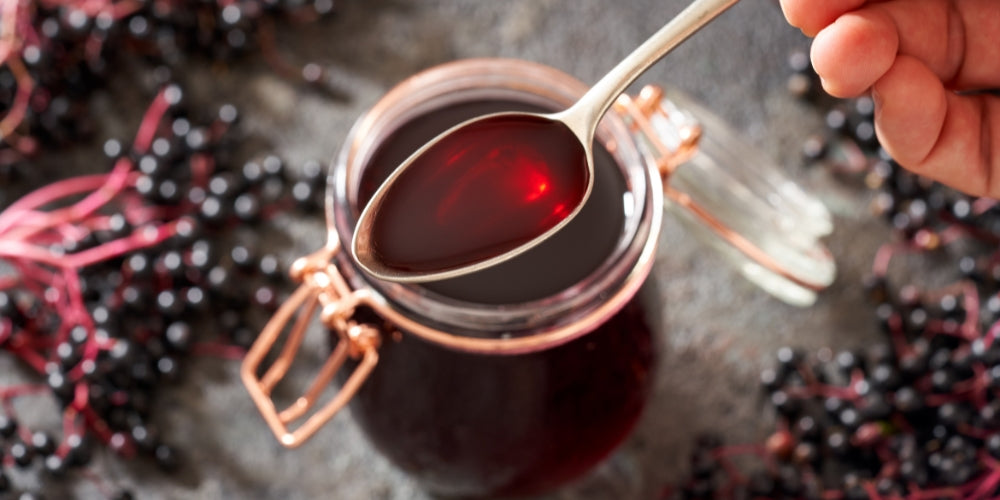 elderberry juice on a spoon surrounded by whole elderberries