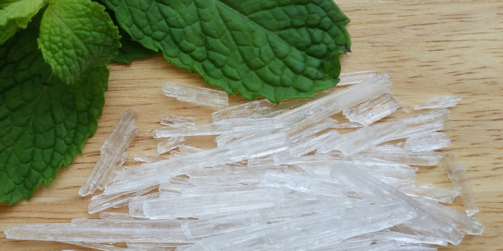 mint leaves with menthol crystals next to it on a wooden table