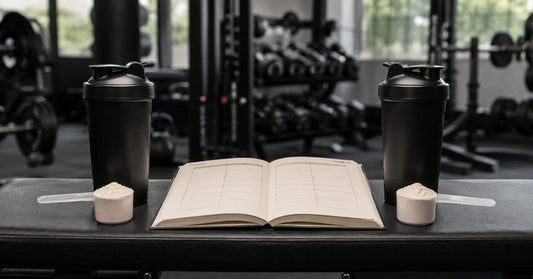 Two black shaker bottles and a blank comparison notebook on a gym bench.